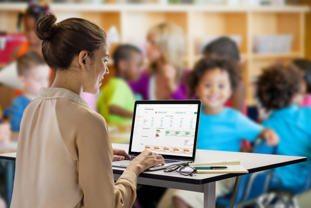 A woman using a laptop with a screenshot of Office on the screen with children in the background, out of focus